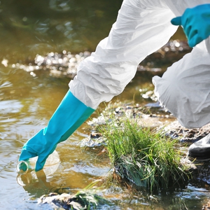 person in protective equipment sampling water